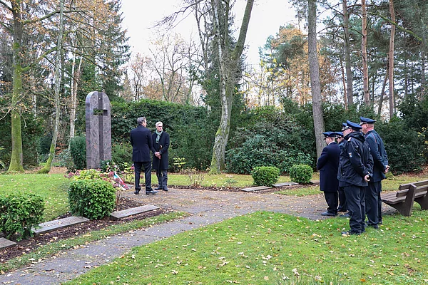 Zwei Männer stehen am Ehrenmal, daneben eine Gruppe der Feuerwehr.