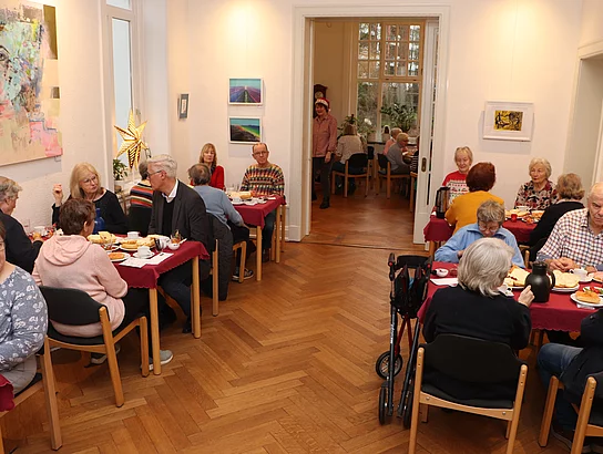 An mehreren weihnachtlichen Tischen sitzen Menschen und frühstücken.