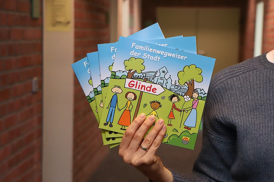 Eine Hand hält mehrere Familienwegweiser in der Hand. Das Cover sieht wie eine bunte Kinderzeichnung aus.