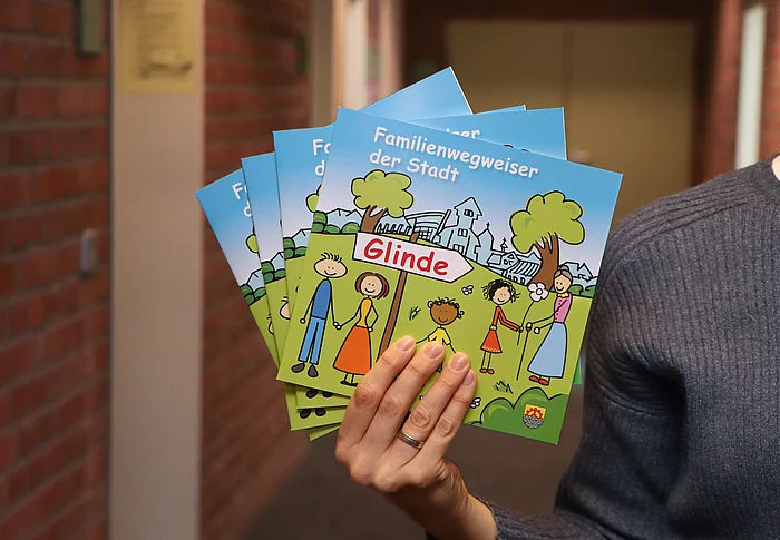 Eine Hand hält mehrere Familienwegweiser in der Hand. Das Cover sieht wie eine bunte Kinderzeichnung aus.
