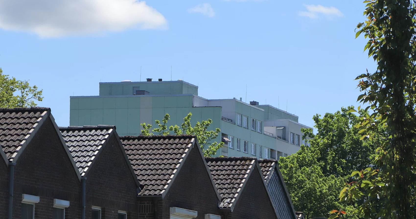 Im Vordergrund Reihenhäuser mit Satteldach, im Hintergrund ein Hochhaus 