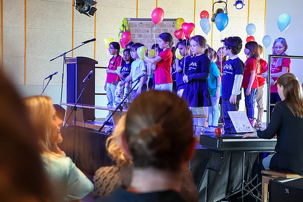 Kinder mit Luftballons stehen auf einer Bühne.