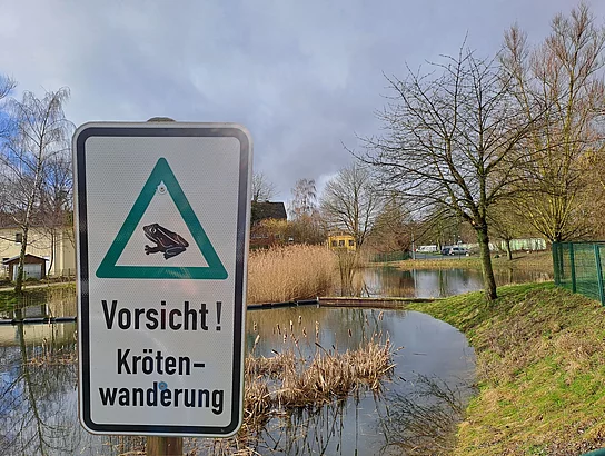 Vor einem Teich steht ein Schild mit der Aufschrift "Vorsicht Krötenwanderung"