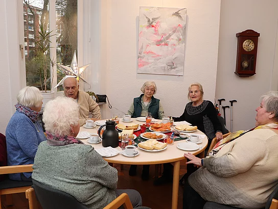 An einem weihnachtlichen Tischen sitzen Menschen und frühstücken.