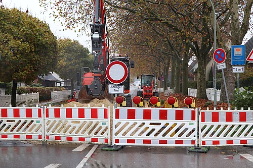 Eine Straße ist mit rot-weissen Absperrelementen blockiert. Dahinter ein Bagger und Baumaterial.