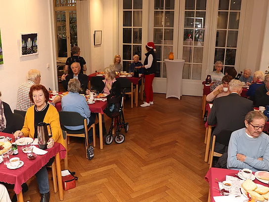 An weihnachtlichen Tischen sitzen Menschen und frühstücken.