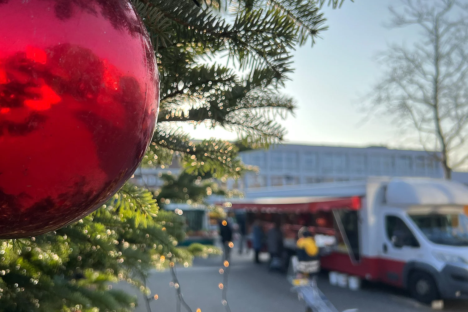 Eine rote Weihnachtsbaumkugel im Vordergrund, im Hintergrund Markttreiben in Glinde