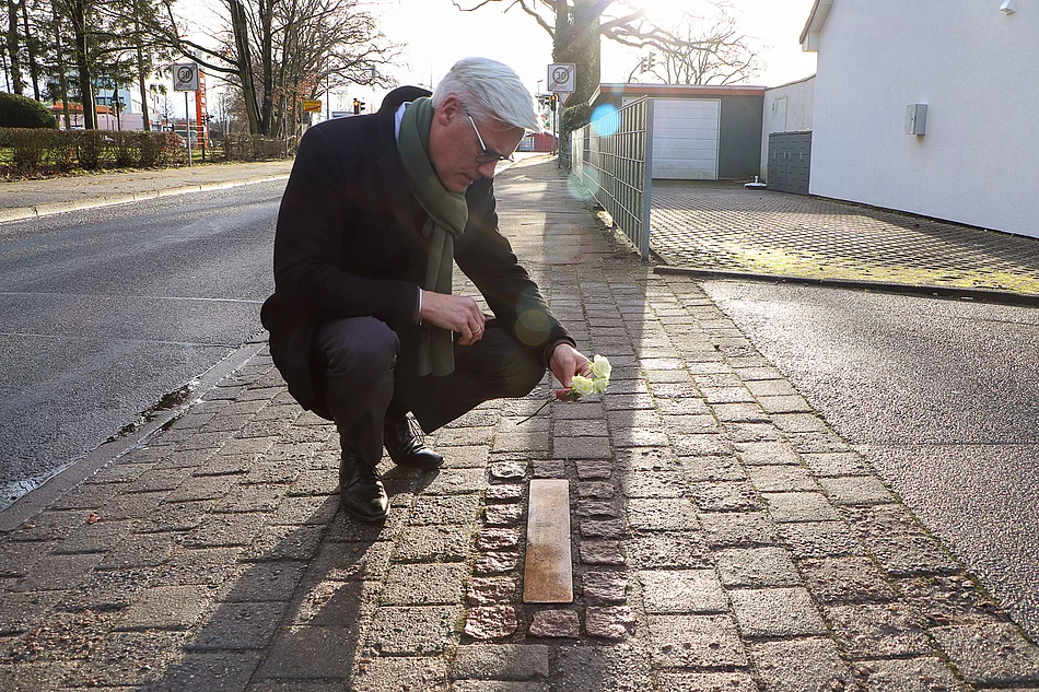 Glindes Bürgermeister Rainhard Zug kniet mit einer weißen Rose an der Stolperschwelle für Zwangsarbeitslager Wiesenfeld.