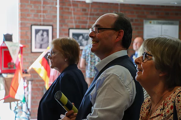 Zwei Frauen und ein Mann schauen auf ein Foto an der Wand.