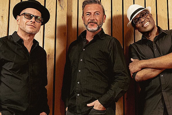 Drei Männer stehen vor einer Wand für ein Bandfoto.