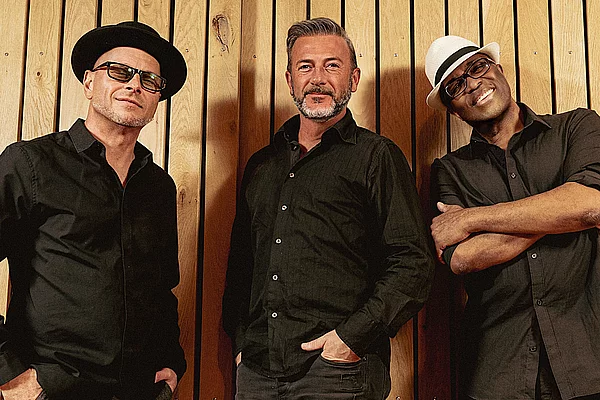 Drei Männer stehen vor einer Wand für ein Bandfoto.