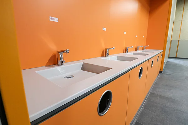 In der Mensa sind in einer orangefarbenen Nische mehrere Waschbecken nebeneinander angebracht.