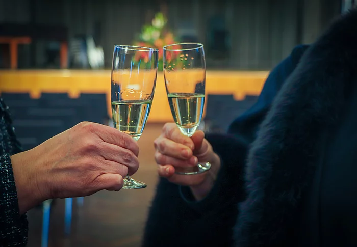 Zwei Hände mit Sektglas stoßen an.