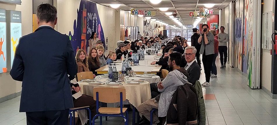 An einem langen Tisch sitzen Schülerinnen und Schüler.