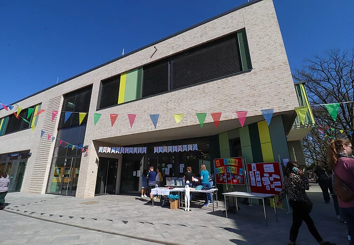 Das Mensa-Gebäude der Grundschule Tannenweg, mit hellem Klinker, dunklen Fenstern und grün-gelben Fassadenelementen.