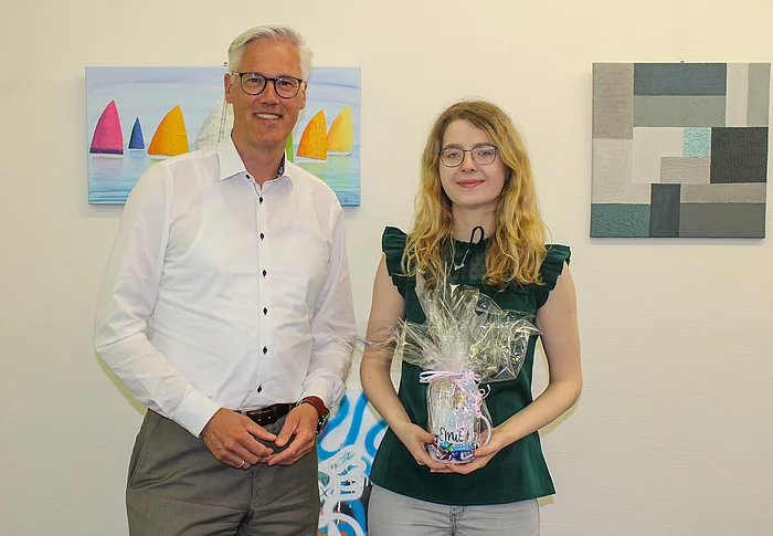 Bürgermeister Rainhard Zug steht neben der ehemaligen Auszubildenden Emily Barth. Sie hält ein Geschenk in den Händen.