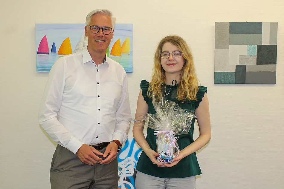 Bürgermeister Rainhard Zug steht neben der ehemaligen Auszubildenden Emily Barth. Sie hält ein Geschenk in den Händen.