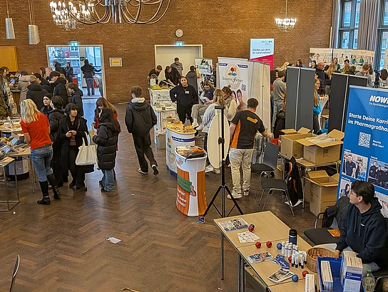 Junge Menschen stehen an Messeständen und unterhalten sich