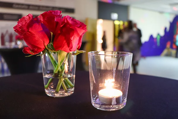 Auf einem Tisch steht ein Teelicht neben roten Rosen.