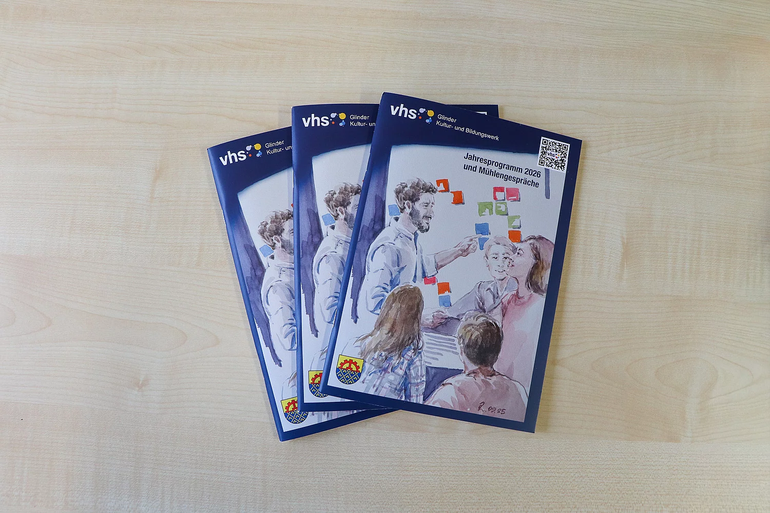 Drei Hefte mit einer Aquarellmalerei liegen auf einem Tisch.