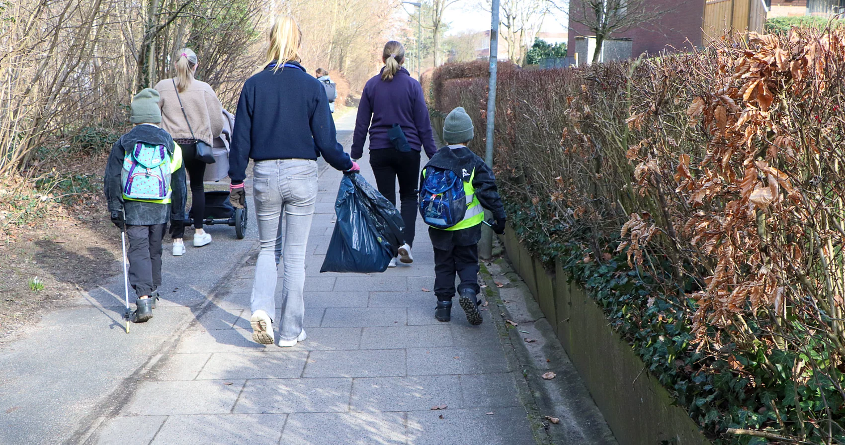 Kinder und Erwachsene gehen einen Weg entlang mit Müllbeuteln.