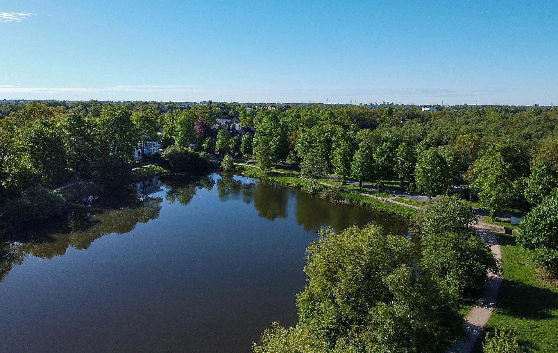 Eine Luftaufnahme des Mühlenteichs mit Blick Richtung Mühle. Es sind viele grüne Bäume zu sehen.