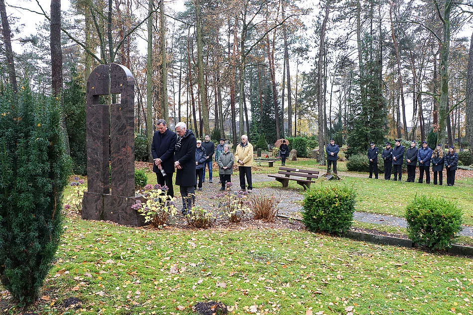 Bürgervorsteher Claus Peters, Bürgermeister Rainhard Zug und weitere Menschen gedenken am Ehrenmal