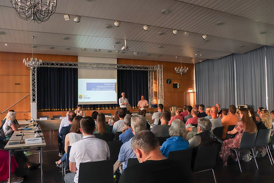 Publikum schaut zu einer Leinwand vor der Bürgermeister Rainhard Zug steht.