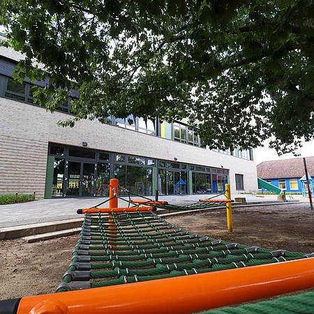 Im Vordergrund eine Hängematte und Spielgeräte, im Hintergrund die Mensa der Grundschule Tannenweg.