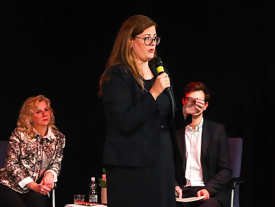 Melanie Lange steht auf der Bühne und hat ein Mikrofon in der Hand.