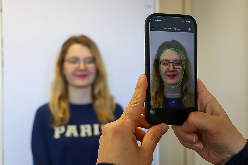 Auf einem Bildschirm eines Smartphones ist das Gesicht einer jungen Frau zu sehen