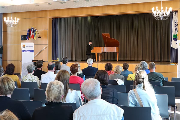 Ein junger Mann spielt auf einer Bühne an einem Flügel. Publikum schaut auf ihn.