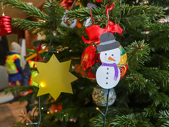 Ein Schneemann aus Papier hängt neben einem gelben Stern aus Papier am Weihnachtsbaum.