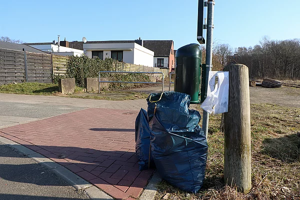 An einem Mülleimer stehen Müllsäcke.