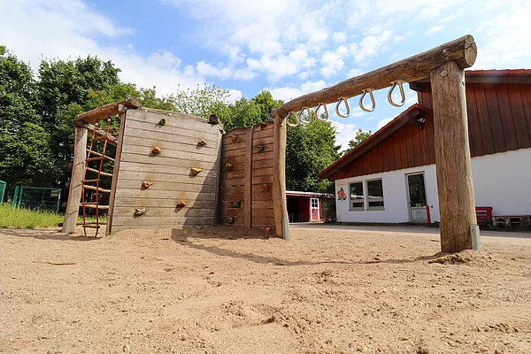 Hinter einer Kletterwand steht das Gebäude des Hort Löwenzahn Wiesenfeld