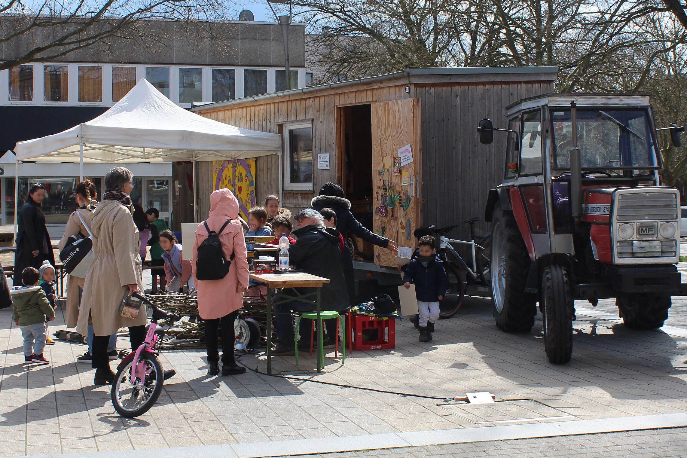 Vor einem roten Traktor mit Bauwagen-Anhänger basteln Kinder.