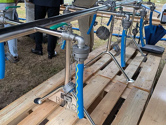 An einem Rohr sind mehrere Wasserhähne mit Schlauch angebracht. 