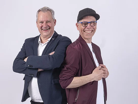 Rudelsingen (Lutz Angermann & Sascha Götz) bringt ein Mitmachkonzert auf die Bühne. Zwei Männer stehen nebeneinander für ein Bandfoto.