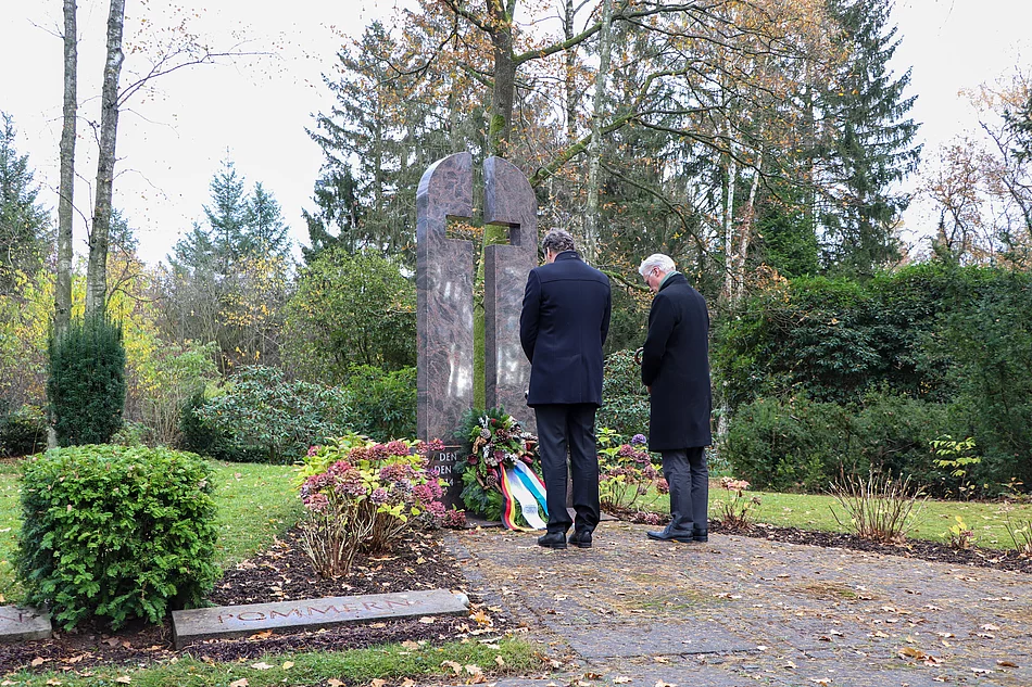 Zwei Männer stehen mit gesenktem Kopf vor dem Ehrenmahl in Form eines Kreuzes auf dem Glinder Freidhof.