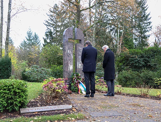 Zwei Männer stehen mit gesenktem Kopf vor dem Ehrenmahl in Form eines Kreuzes auf dem Glinder Freidhof.