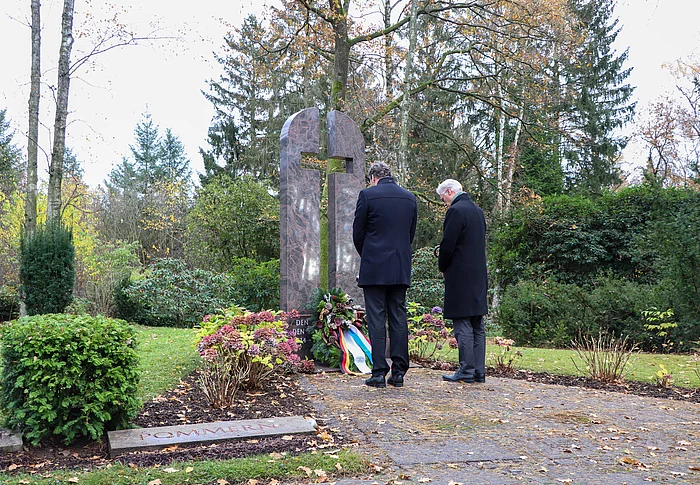 Zwei Männer stehen mit gesenktem Kopf vor dem Ehrenmahl in Form eines Kreuzes auf dem Glinder Freidhof.