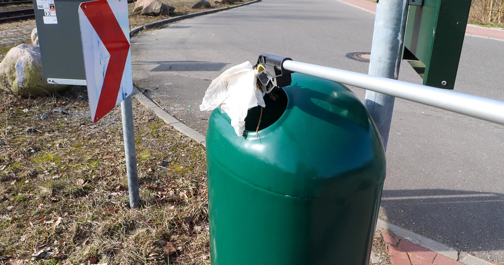 Ein grüner Mülleimer in den mit eine Zange Müll geworfen wird.