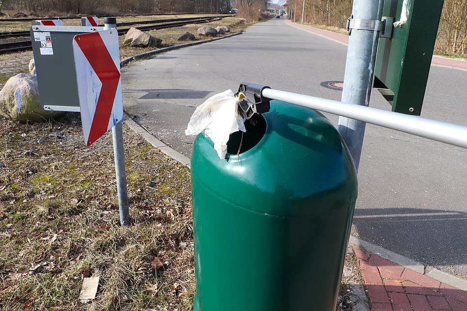 Ein grüner Mülleimer in den mit eine Zange Müll geworfen wird.