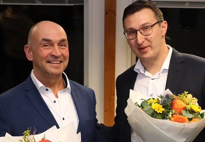 Zwei Männer halten Blumensträuße und lächeln.