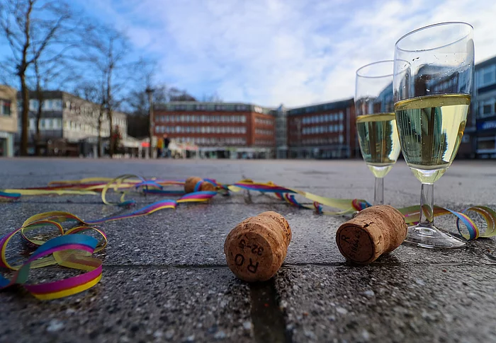 Zwei gefüllte Sektgläser, Korken und Luftschlangen liegen auf dem Markt mit dem Rathaus im Hintergrund.