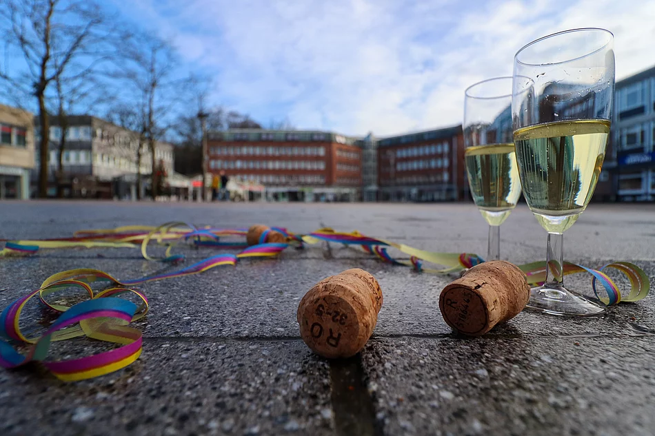 Zwei gefüllte Sektgläser, Korken und Luftschlangen liegen auf dem Markt mit dem Rathaus im Hintergrund.