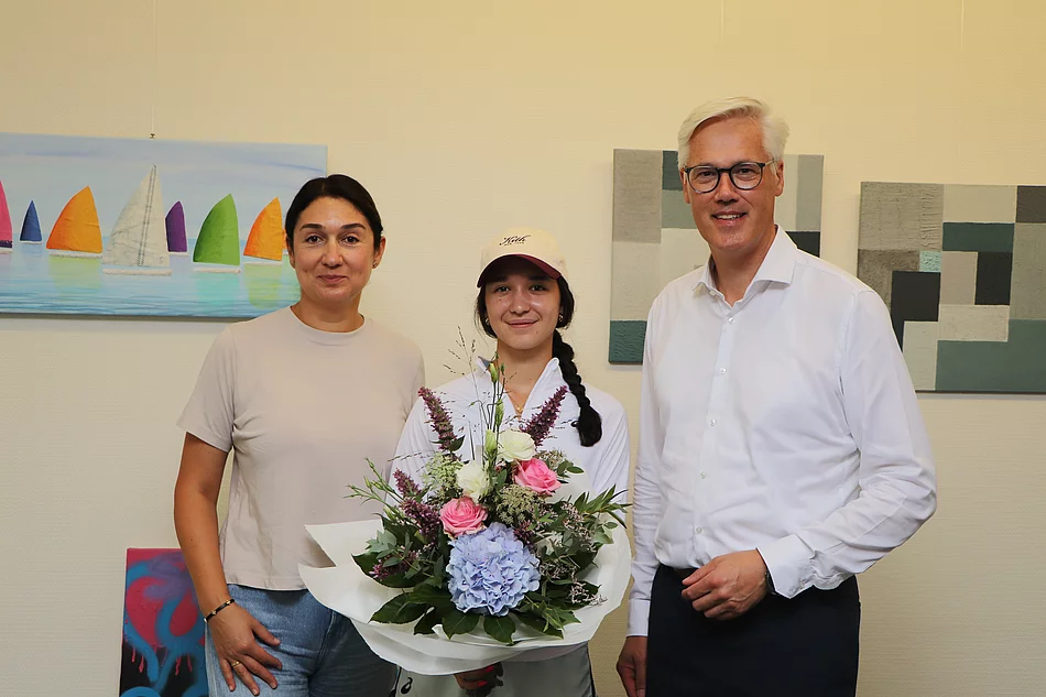 Profi-Tennisspielerin Eva Lys in der Mitte hat einen Blumenstrauß in der Hand, links neben ihr seht ihre Mutter Maria und rechts neben Eva steht Bürgermeister Rainhard Zug