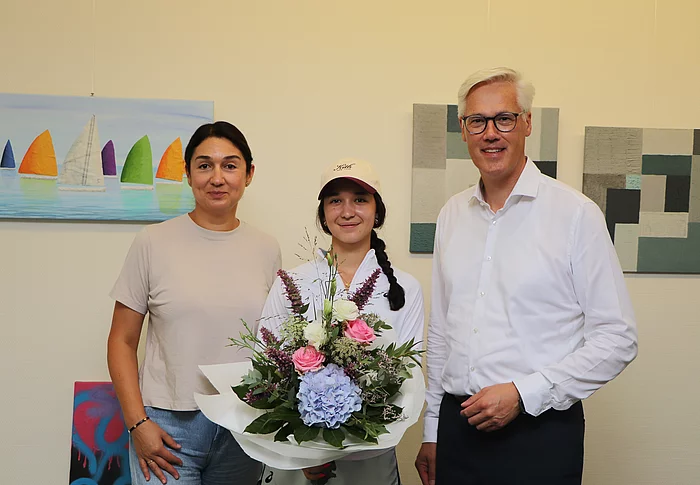 Profi-Tennisspielerin Eva Lys in der Mitte hat einen Blumenstrauß in der Hand, links neben ihr seht ihre Mutter Maria und rechts neben Eva steht Bürgermeister Rainhard Zug