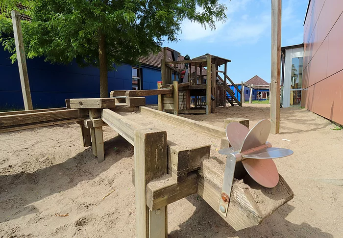 Spielplatz: Im Vordergrund ein Mühlenrad, das von Wasser angetrieben werden kann, hinten eine Wasserstrecke aus Holz gebaut.