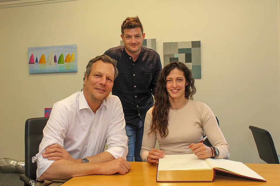 Drei Menschen an einem Schreibtisch. Die Frau hat einen Stift und das Goldene Buch der Stadt vor sich.
